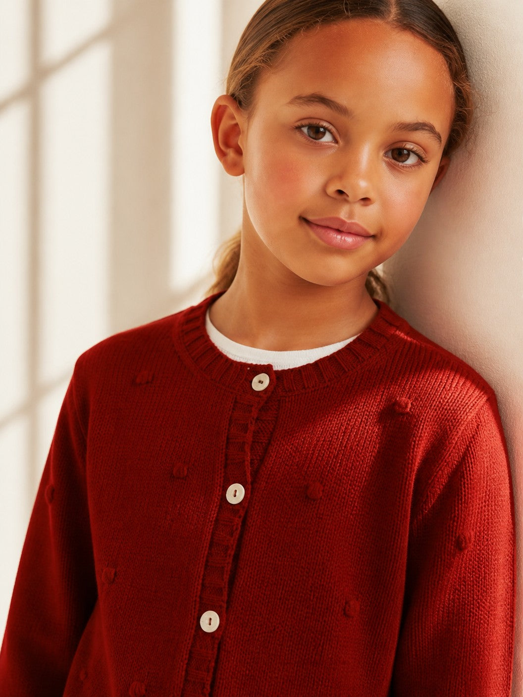 Bambina indossa un cardigan Scaldacuore rosso in maglia con bottoni frontali e dettagli a rilievo