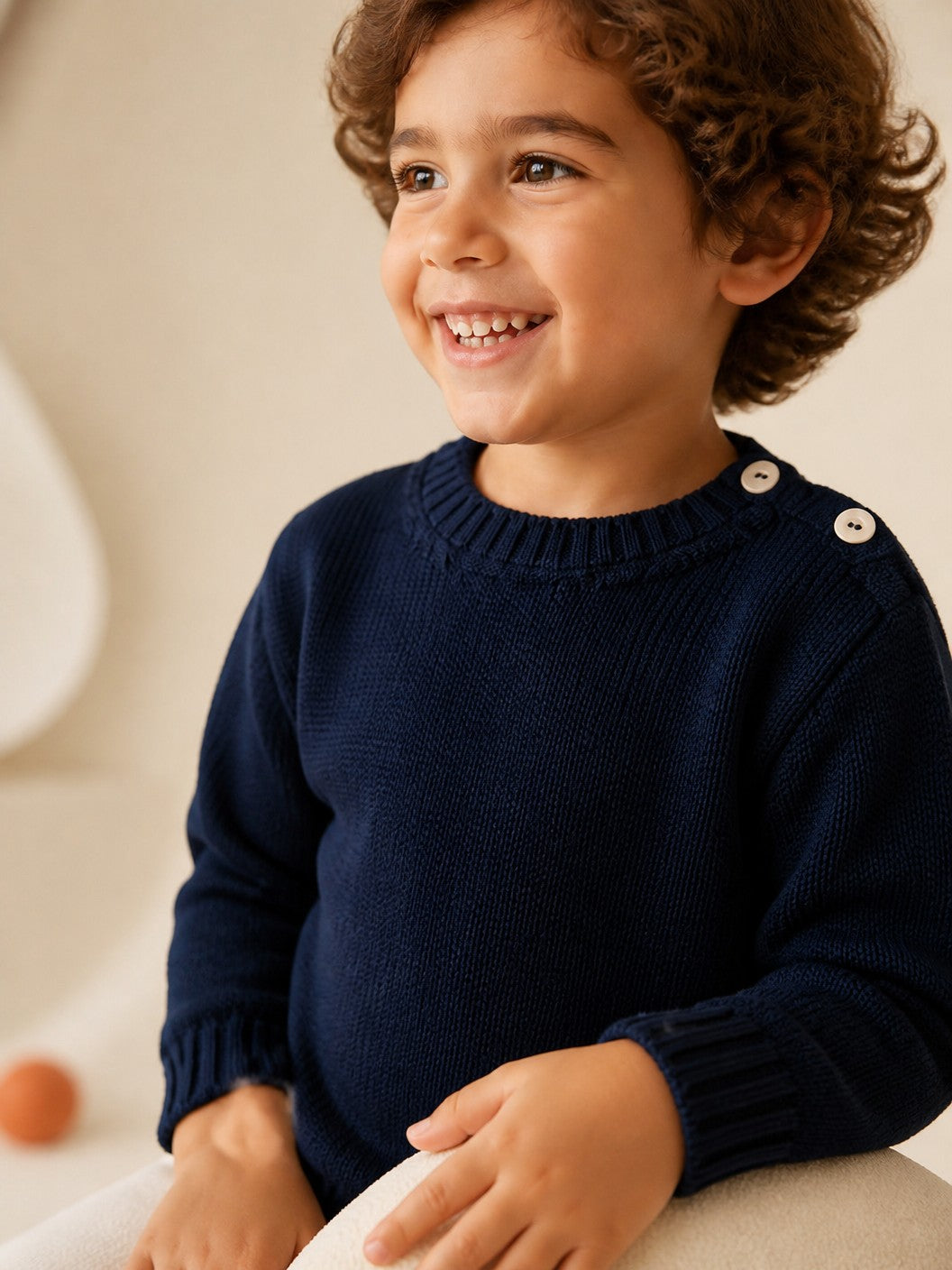Bambino sorridente indossa un girocollo Scaldacuore in lana merino blu denim con bottoni sulla spalla e trama trapuntata