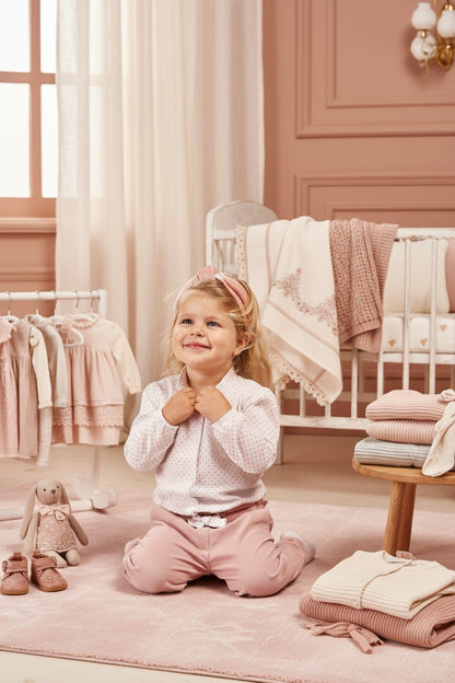Bambina Scaldacuore indossa camicia bianca in cotone con pallini rosa e bottoni in madreperla in una stanza elegante.