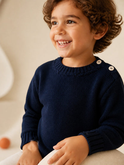 Bambino sorridente indossa un girocollo Scaldacuore in lana merino blu denim con bottoni sulla spalla e trama trapuntata